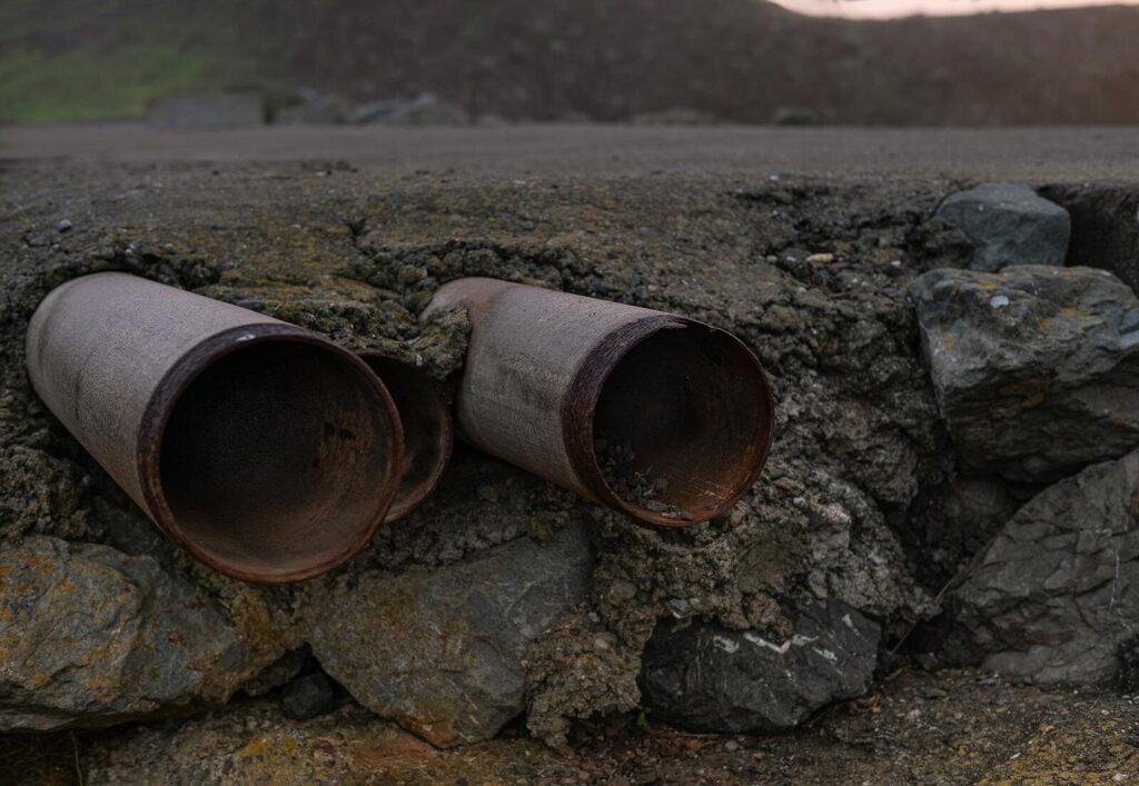 Close-up of two rusty steel pipes protruding from a rocky surface, showcasing erosion and weathering effects.