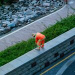 City gardener in orange uniform tending to plants on a stone wall in a park.