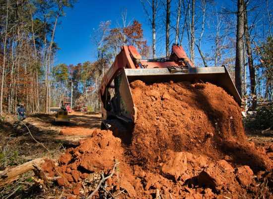 Skid steer loader moving dirt in a wooded area