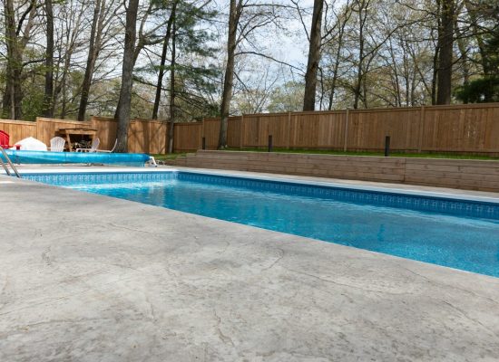 A backyard pool with wood fence and trees.