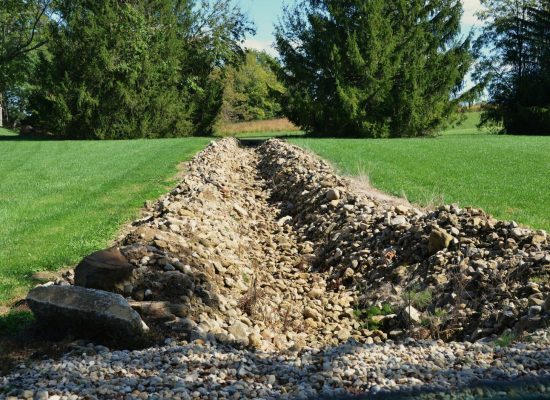Trench dug in a grassy yard with rocks